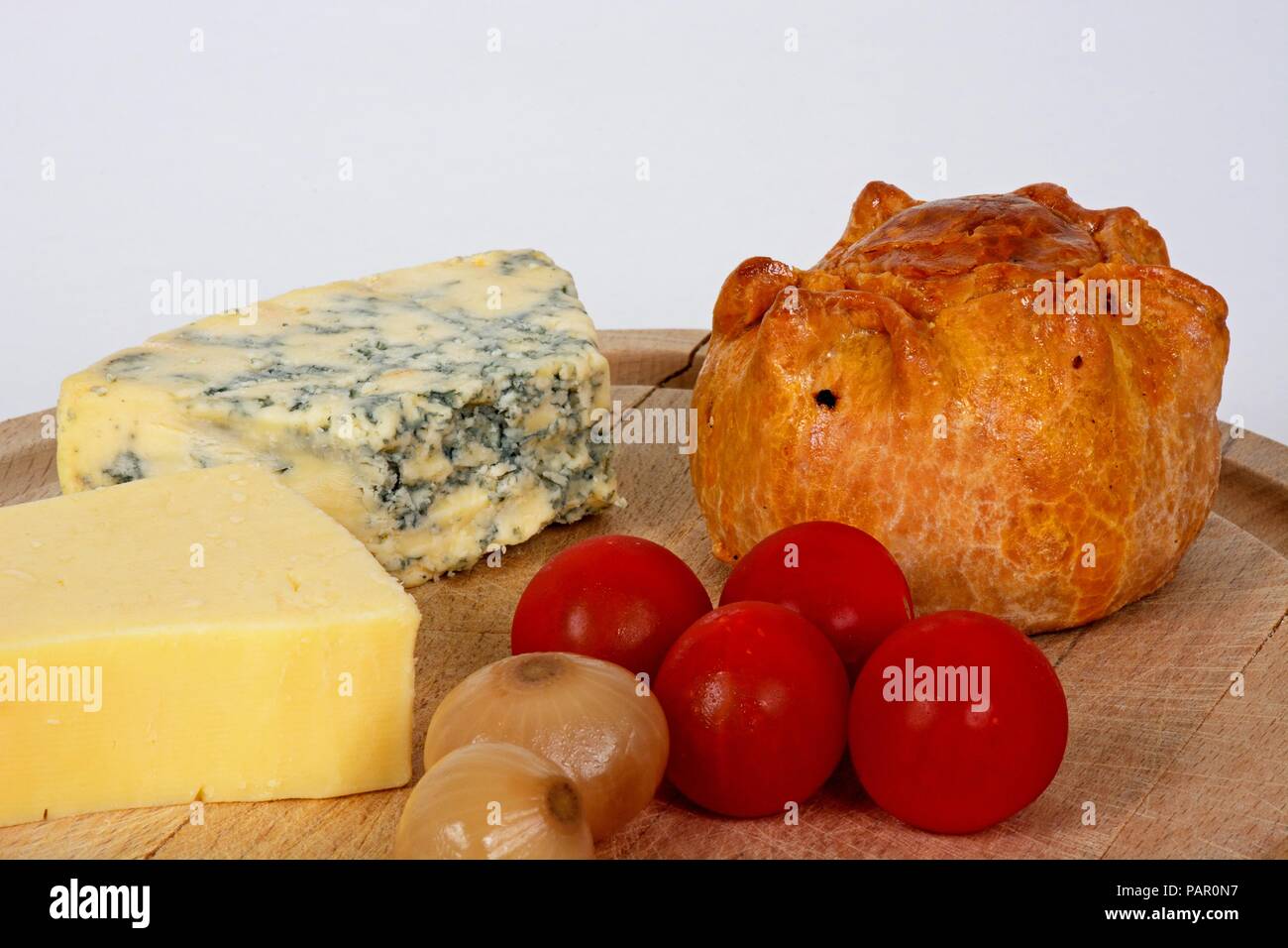 Plowmans Mittagessen auf einem Holzbrett bestehend aus Pork Pie, Stilton Cheese, Cheddar Käse, Tomaten und eingelegte Zwiebeln, England, UK, Europa. Stockfoto