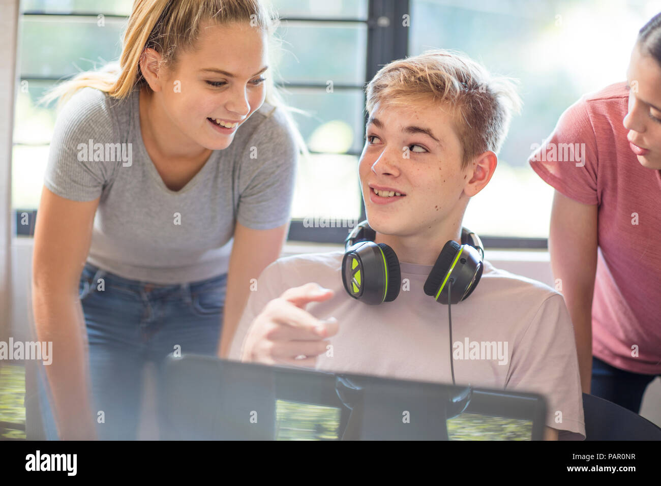 Mädchen im Teenageralter im Gespräch mit Jungen mit Laptop Stockfoto