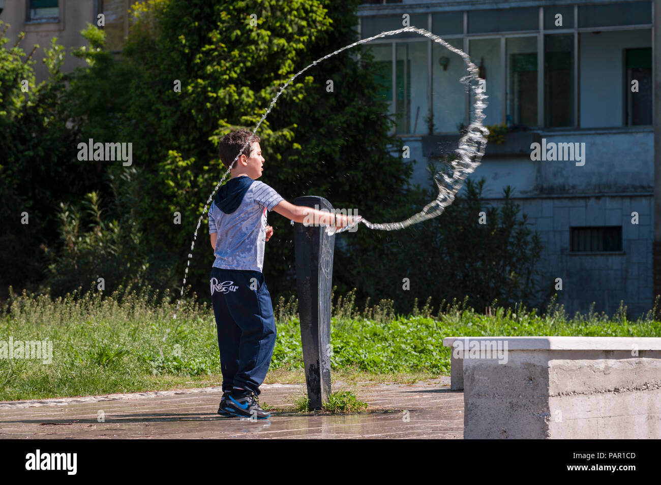 Venedig, Italien. Ein Junge spielt mit einem Trinkbrunnen, werfen Wasser aus einer Flasche einen Kreis von Wasser in der Luft zu machen Stockfoto