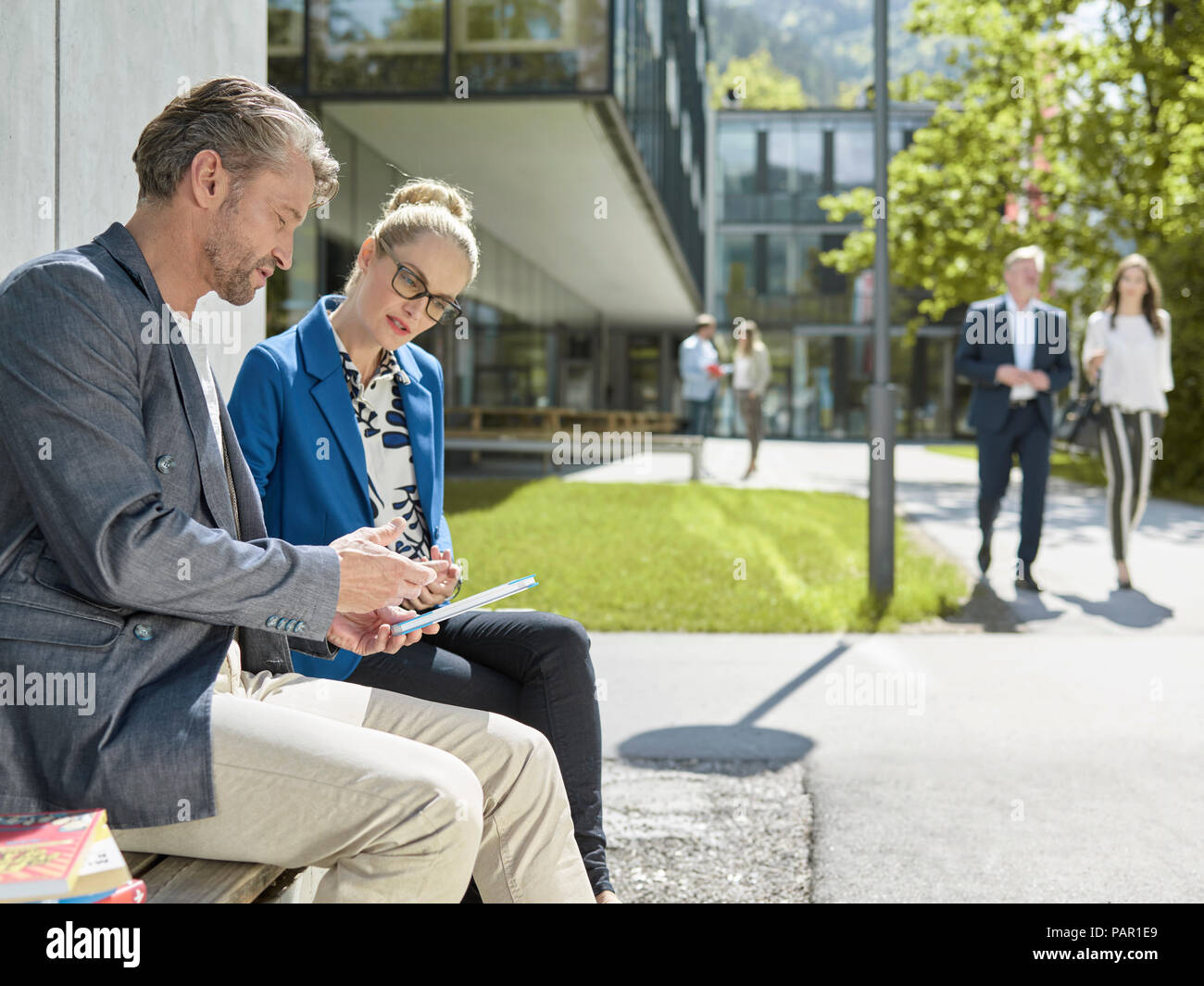 Kollegen mit Tablet sitzt auf der Bank außerhalb der Gebäude Stockfoto