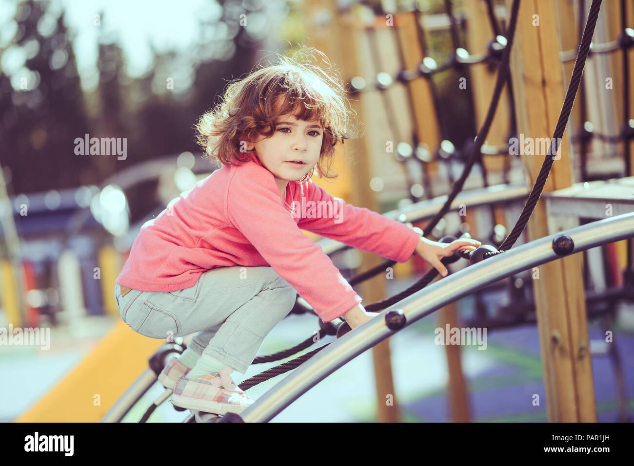 Portrait von kleinen Mädchen kauert auf klettergerüst am Spielplatz Stockfoto