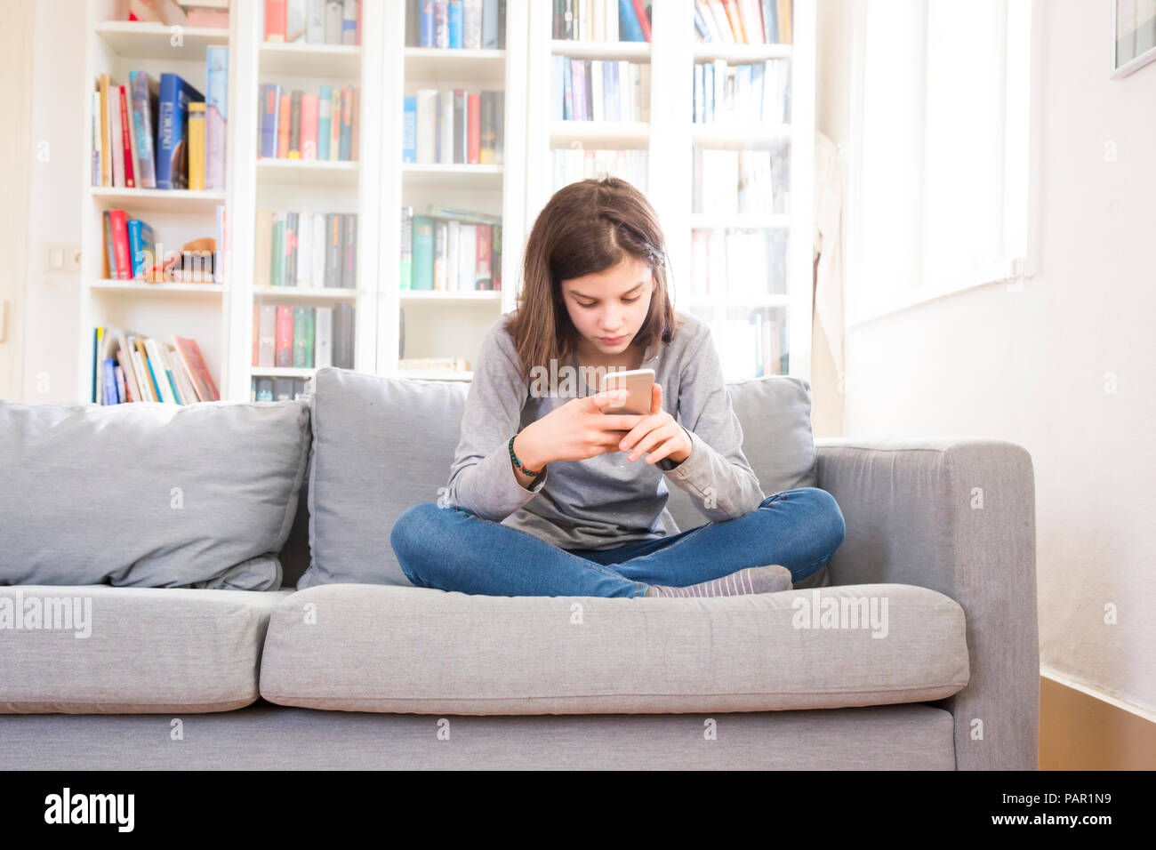 Mädchen sitzen auf der Couch zu Hause mit Handy Stockfoto