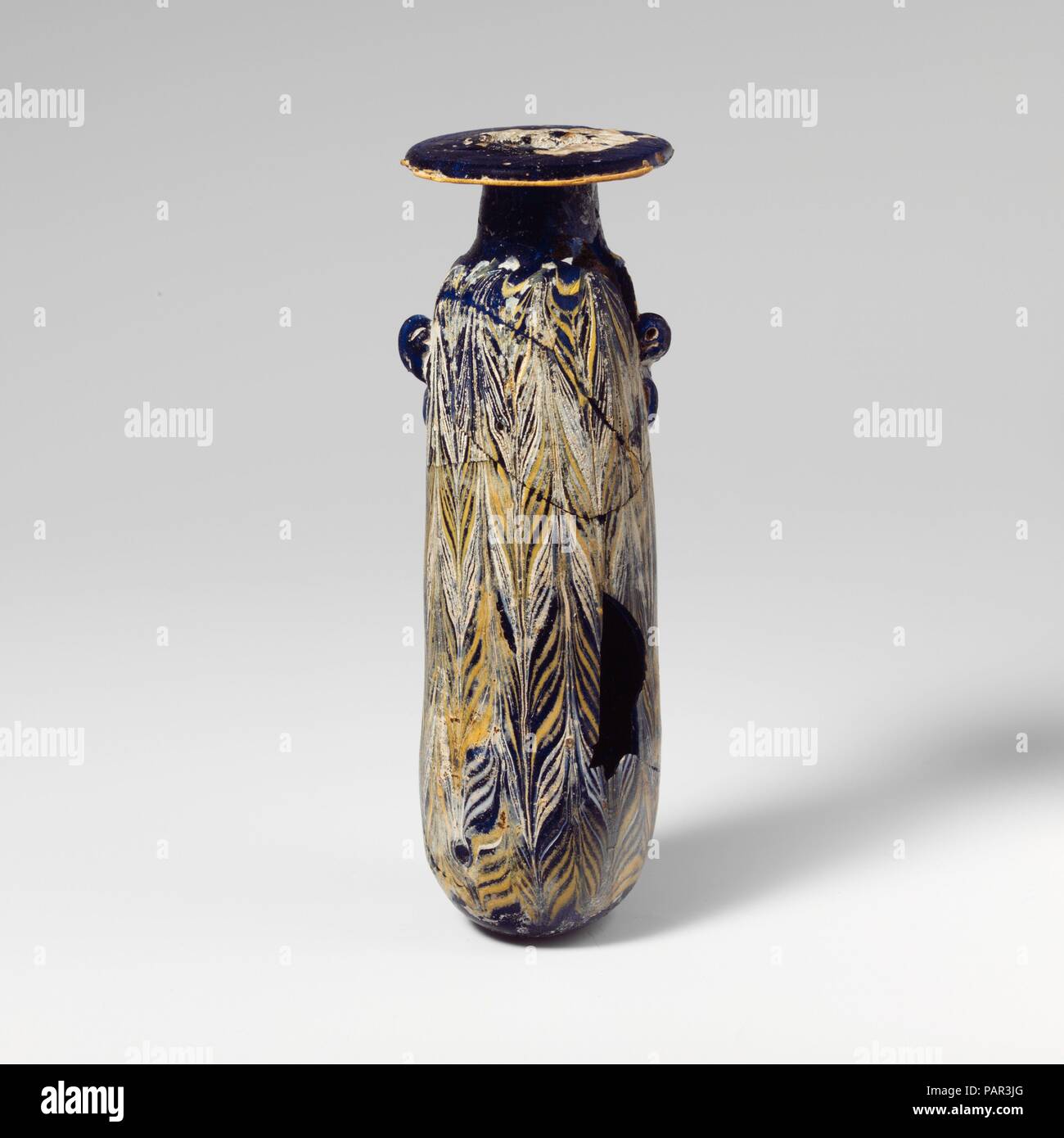 Glas alabastron (Parfüm Flasche). Kultur: Griechisch, Östliches Mittelmeer oder Italienisch. Abmessungen: H.: 5 5/8 in. (14,3 cm). Datum: Mitte 4.-Anfang 3.Jh. v. Chr.. Transluzente Kobaltblau, mit Griffen in der gleichen Farbe; Wanderwege in opak Gelb und Deckweiß. Breite horizontale Rim-disk, schräge leicht nach außen; zylindrische Hals, nach unten erweitert; schmale abgerundete Schulter; Gerade-seitig zylindrische Körper, mit leicht nach oben Konus; konvexen Boden; unterhalb der Schulter, zwei vertikale ring Griffe, nicht durch, durchbohrt mit kurzen spitzen Wanderwege, über trail Muster angewendet. Eine feine gelbe Weg befestigt, die an Stockfoto