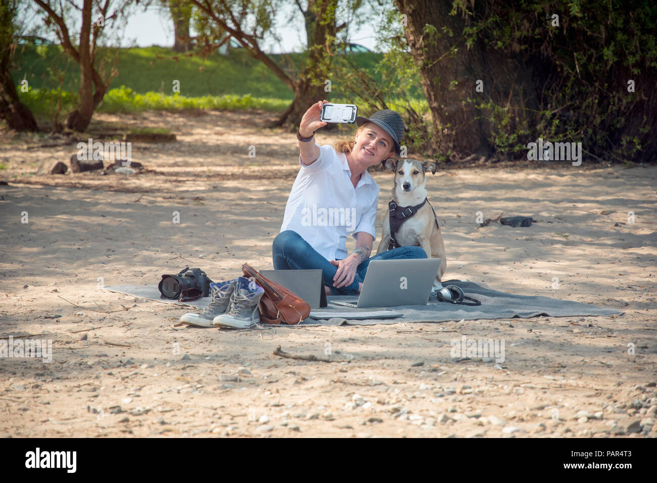Lächelnde Frau sitzt auf der Decke am Strand mit Hund eine selfie Stockfoto