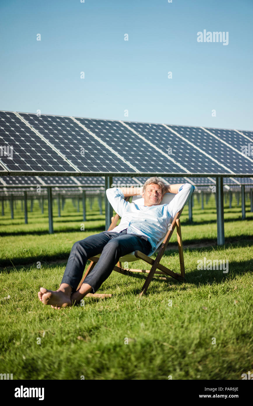 Reifer Mann sitzt im Liegestuhl, Solaranlage Stockfoto