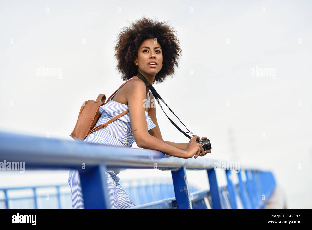 Portrait von modische junge Frau mit Rucksack und Kamera steht auf einer Brücke Stockfoto