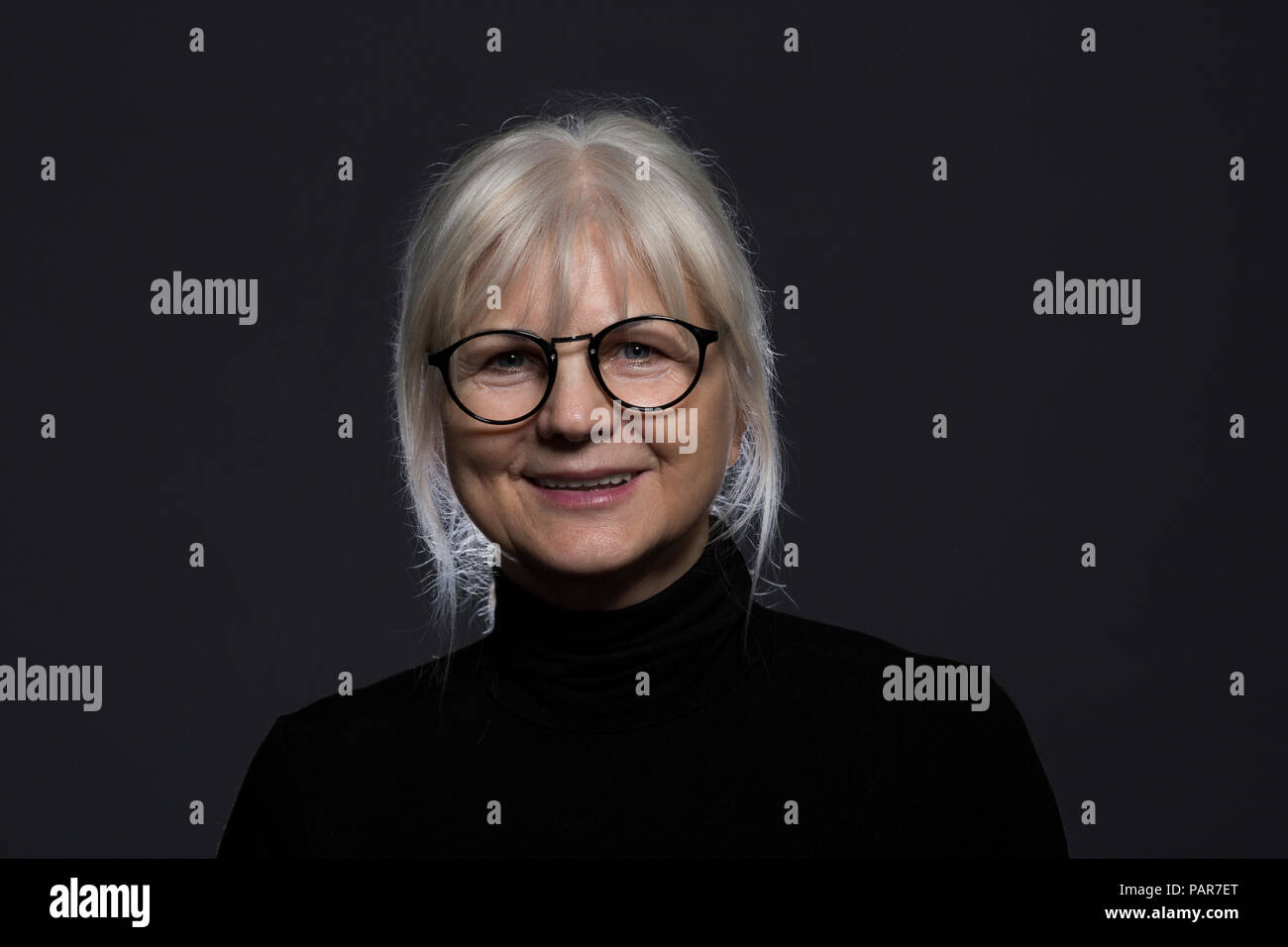 Portrait von lächelnden älteren Frau mit Brille vor dunklem Hintergrund Stockfoto