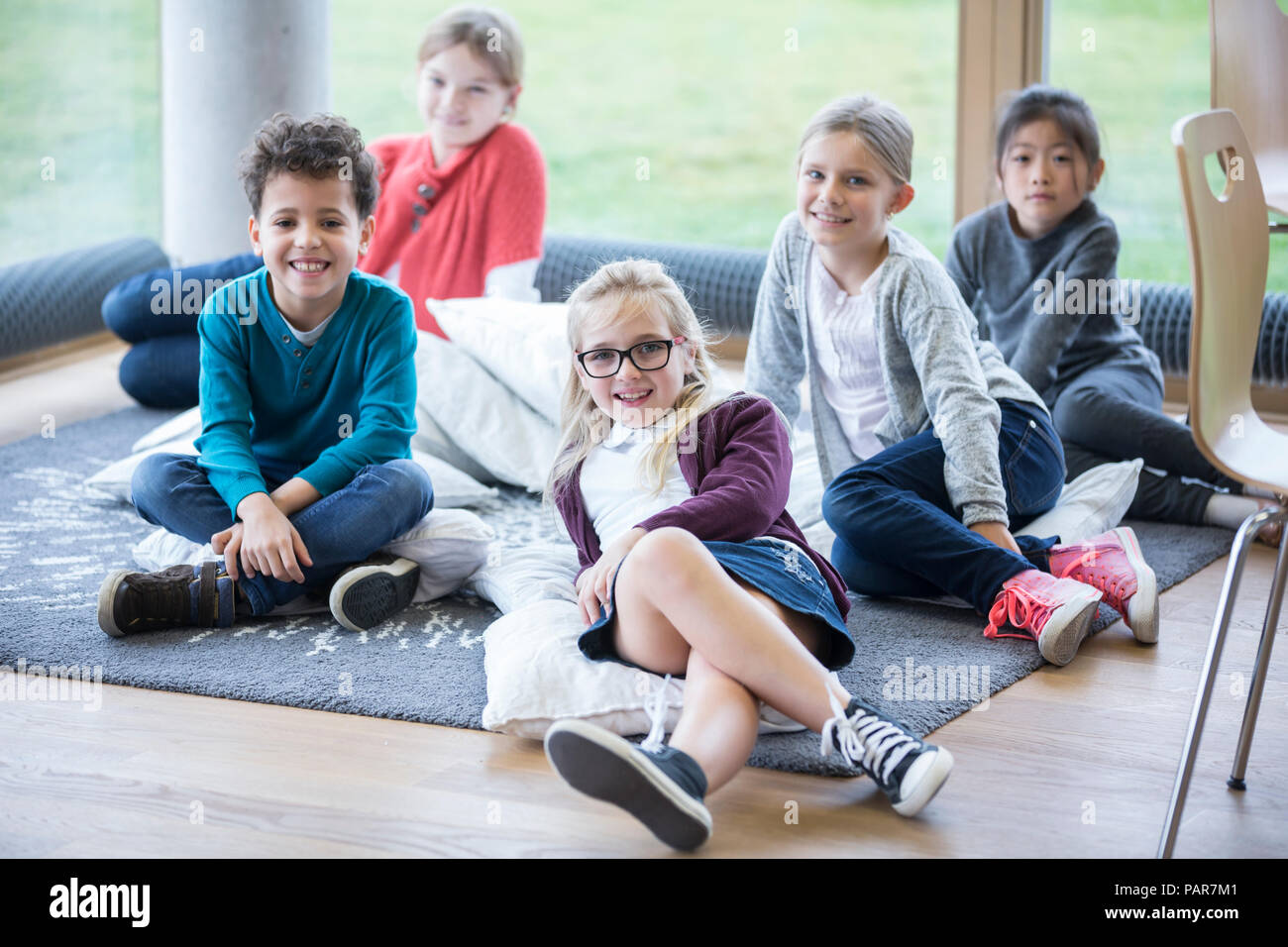 Portrait von lächelnden Schüler sitzen auf dem Boden in der Schule pause Zimmer Stockfoto