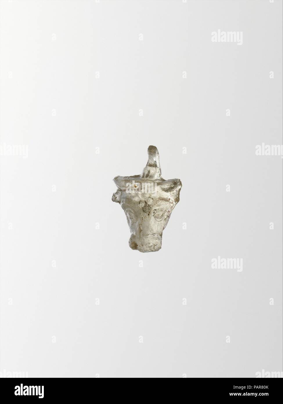 Glas Anhänger in der Form des Kopfes ein Stier. Kultur: Griechisch, östlichen Mittelmeer. Abmessungen: H.: 13/16-in. (2,1 cm). Datum: Ende 2nd-1st Jahrhundert v. Chr.. Farblos. Solide, vertikale Anhänger, mit Schimmel Markierungen, an den Seiten und oben von Kopf und über Schleife; auf der Oberseite des Kopfes, eine kleine vertikale Dämpfung Schleife; flache Rückseite mit kleinen zentralen Bohrung. Leiter der Stier, mit Hörnern und Ohren, markanten Augenbrauen und Ausbauchende Augen; Stern Rosette auf der Stirn. Intakt, aber um die Kanten gesäumt; einige Lochfraß und schwache irisierende Verwitterung. Museum: Metropolitan Museum of Art, New York, USA. Stockfoto