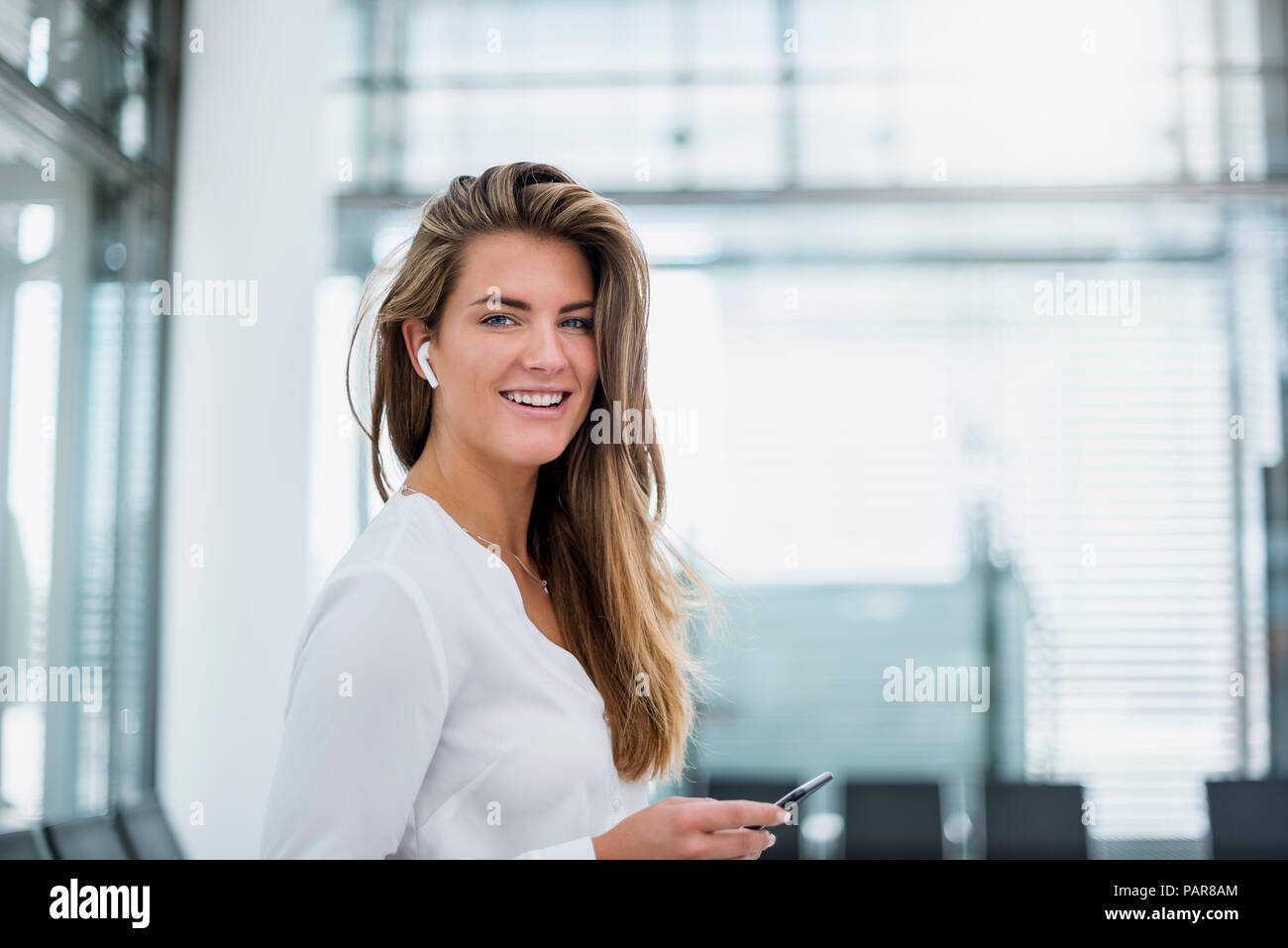 Lächelnden jungen Frau das Tragen im Ohr mit Handy Telefon Stockfoto