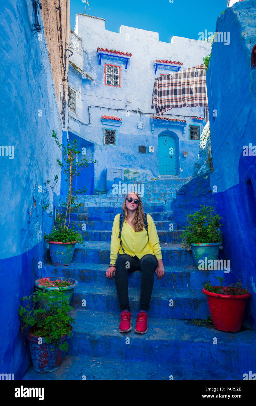 Junge Frau sitzt auf der Treppe in der Altstadt, blaues Haus Fassaden, Medina von Meknes, Chaouen, Tangier-Tétouan, Marokko Stockfoto