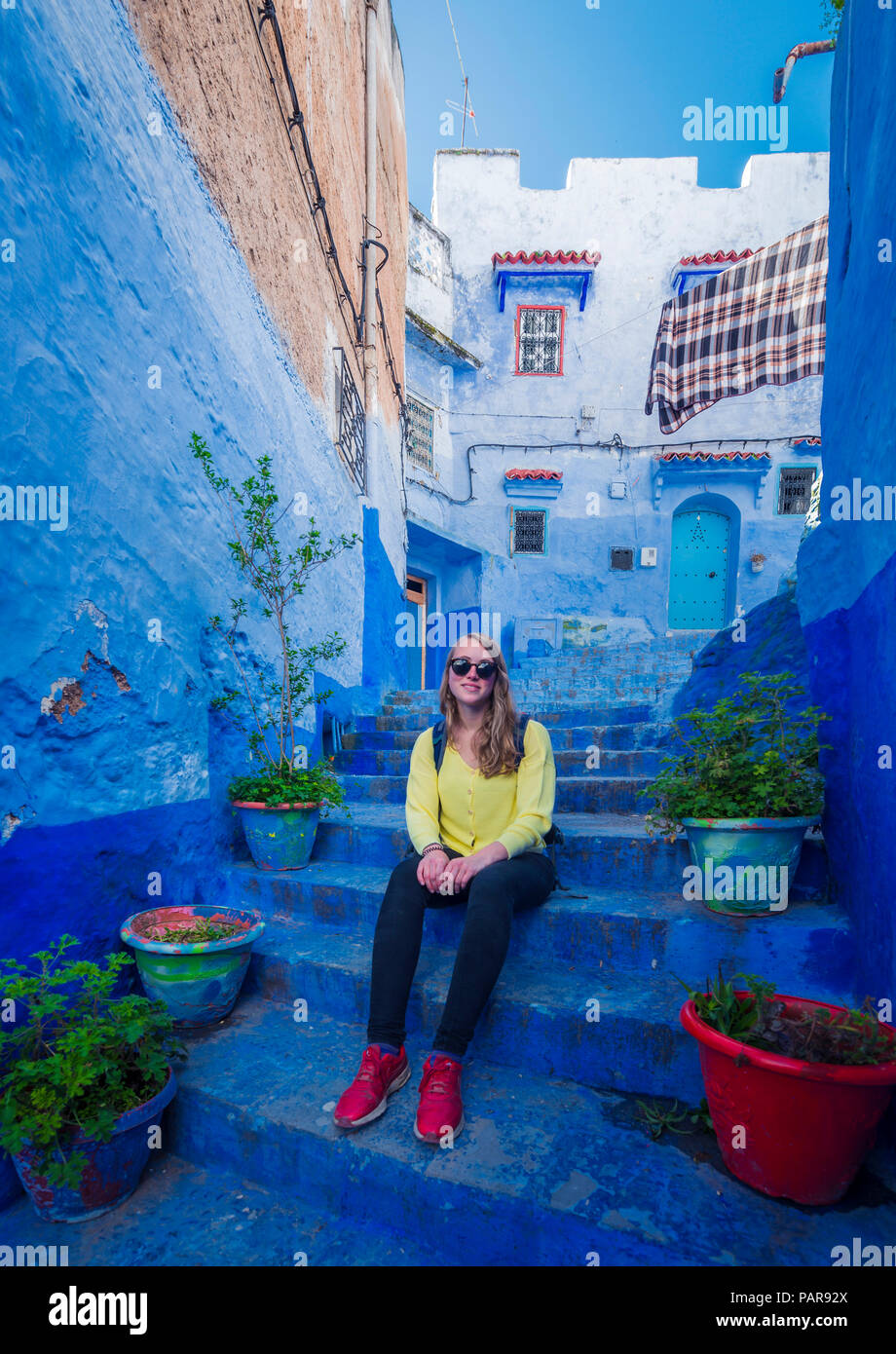 Junge Frau sitzt auf der Treppe in der Altstadt, blaues Haus Fassaden, Medina von Meknes, Chaouen, Tangier-Tétouan, Marokko Stockfoto