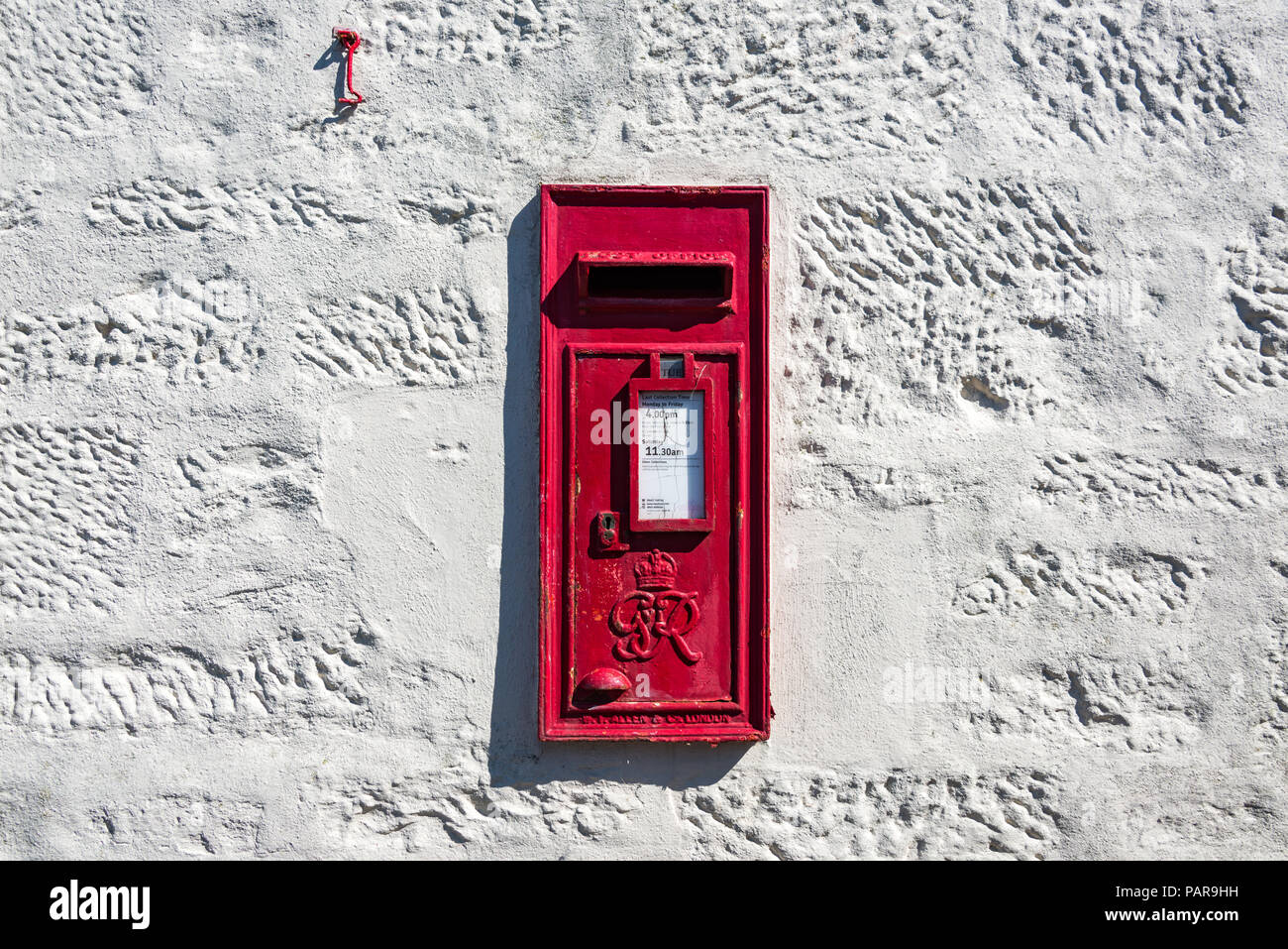 Ein roter Briefkasten, der in eine weiß getünchte Steinmauer in England, Großbritannien, gesetzt wurde Stockfoto