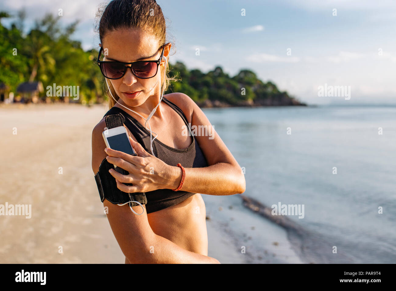 Thailand, Koh Phangan, sportliche Frau, die während des Trainings am Strand, Smartphone Stockfoto