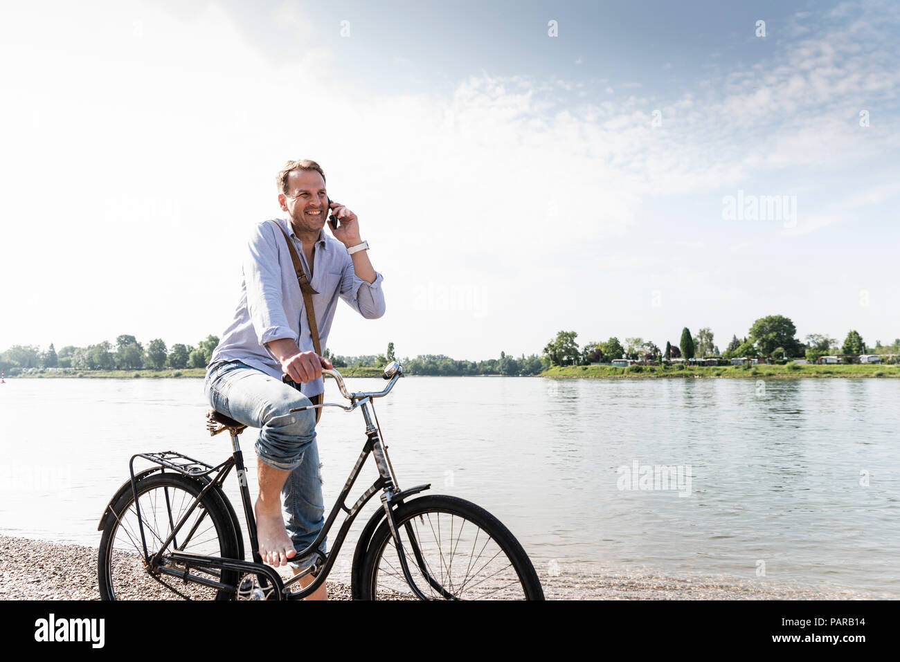 Reifer Mann mit Fahrrad mit an Rhein Ufer smartphone Stockfoto