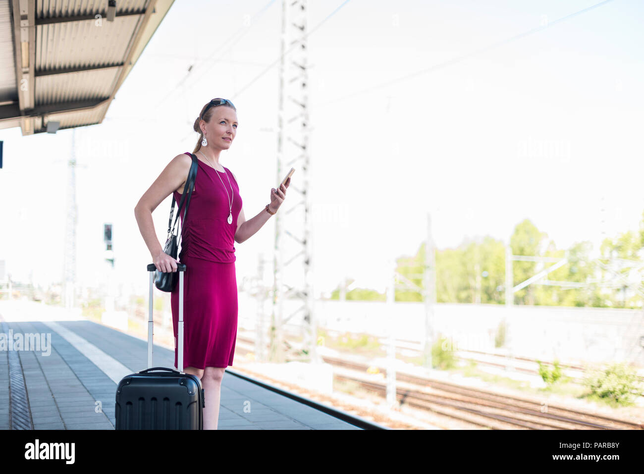 Reife Geschäftsfrau mit Koffer und Smartphone warten an Plattform Stockfoto