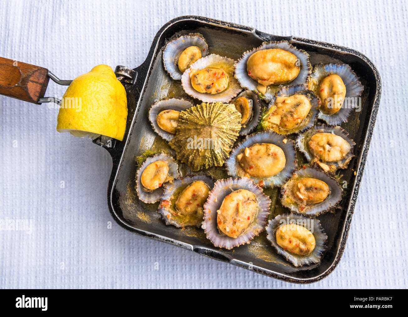 Gegrillte napfschnecken in der Pfanne mit Zitrone serviert. Stockfoto