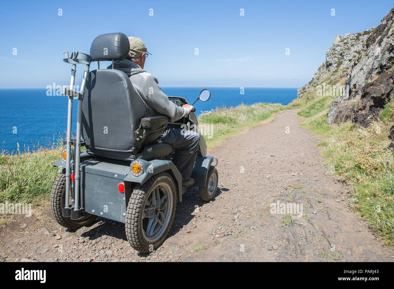 Ein älterer Mann reiten auf einem Mobilität scooter oder tramper auf rauem Gelände auf dem Land und an der Küste Stockfoto