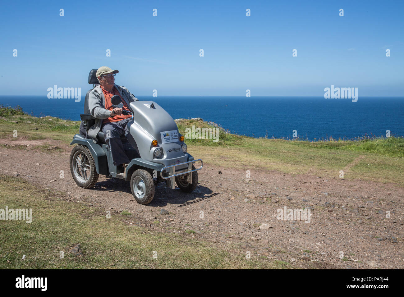 Ein älterer Mann reiten auf einem Mobilität scooter oder tramper auf rauem Gelände auf dem Land und an der Küste Stockfoto