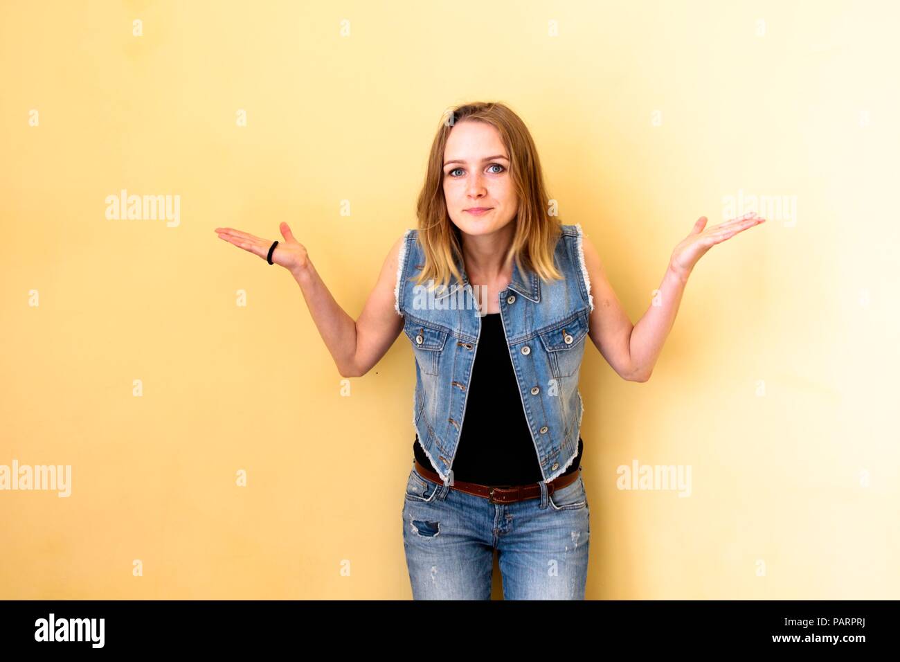 Schöne Mädchen mit ihrem Haar, stehend auf einem gelben Hintergrund. Sie weiß nicht, was passiert ist und zeigt, dass es mit Ihrem ganzen Hände. Stockfoto