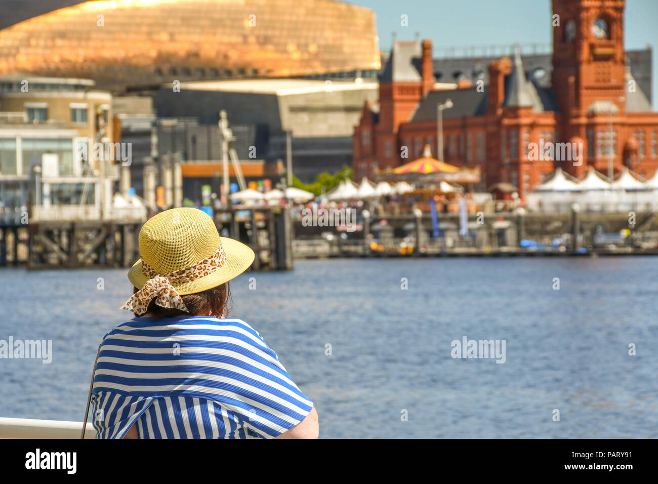 Frau mit Sonnenhut lehnte sich auf Geländer über Cardiff Bay in Richtung Wahrzeichen am Wasser. Stockfoto