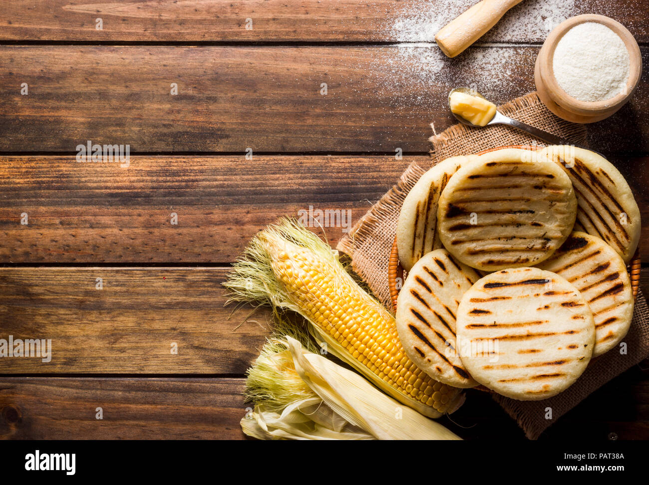 Blick von oben aus Holz im Landhausstil Tabelle mit mehreren Boden mais Arepas, einige Mais und Butter, alle Objekte sind auf der rechten Seite des Bildes leavi Stockfoto