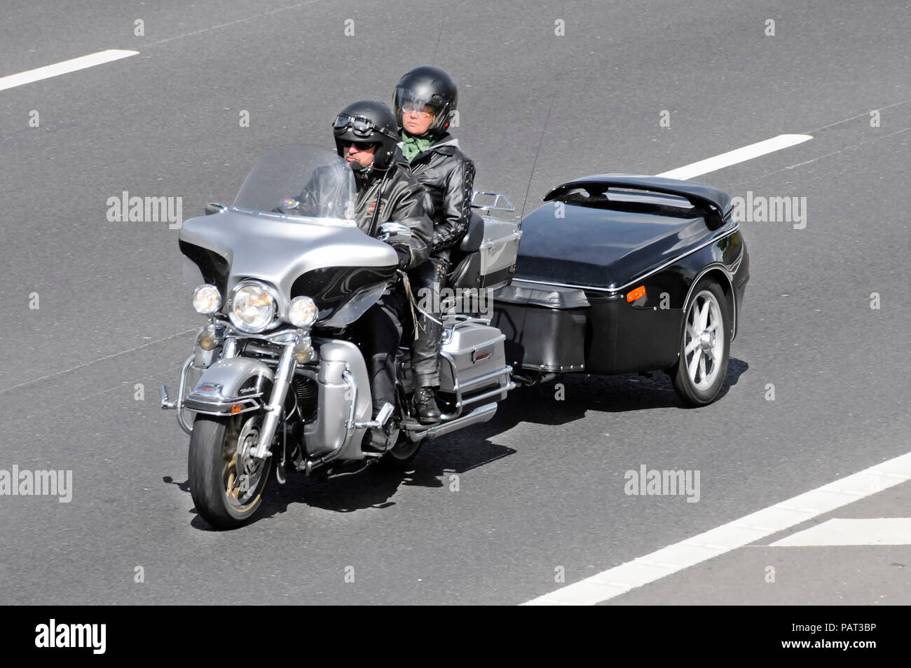 Männliche Motorradfahrer tragen Mikrofon & Frau reiten Motorrad Sozius Paar tragen Helm abschleppen ungewöhnliche Anhänger Auf de Autobahn Stockfoto