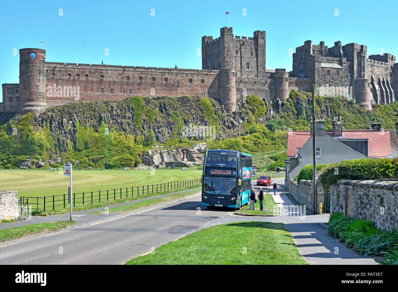 Tourismus & ländliche Double Decker Bus Öffentliche Verkehrsmittel Haltestelle Bamburgh Village Green & historische Bamburgh Castle Northumberland, England Großbritannien Stockfoto