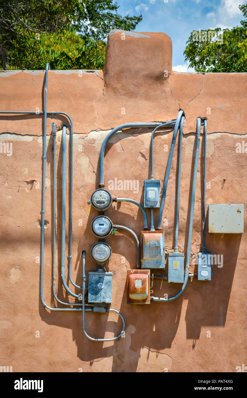 Einen künstlerischen Blick auf alte, rostige, grungy, elektrische Meter geclustert und planlos auf alten Adobe Gebäude installiert Stockfoto
