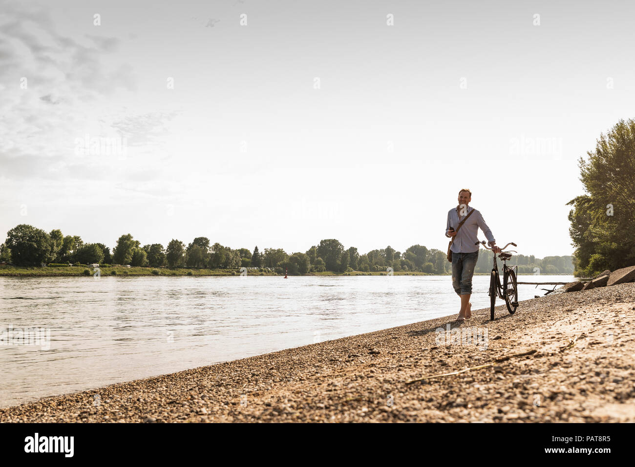 Reifer Mann mit Fahrrad mit an Rhein Ufer smartphone Stockfoto