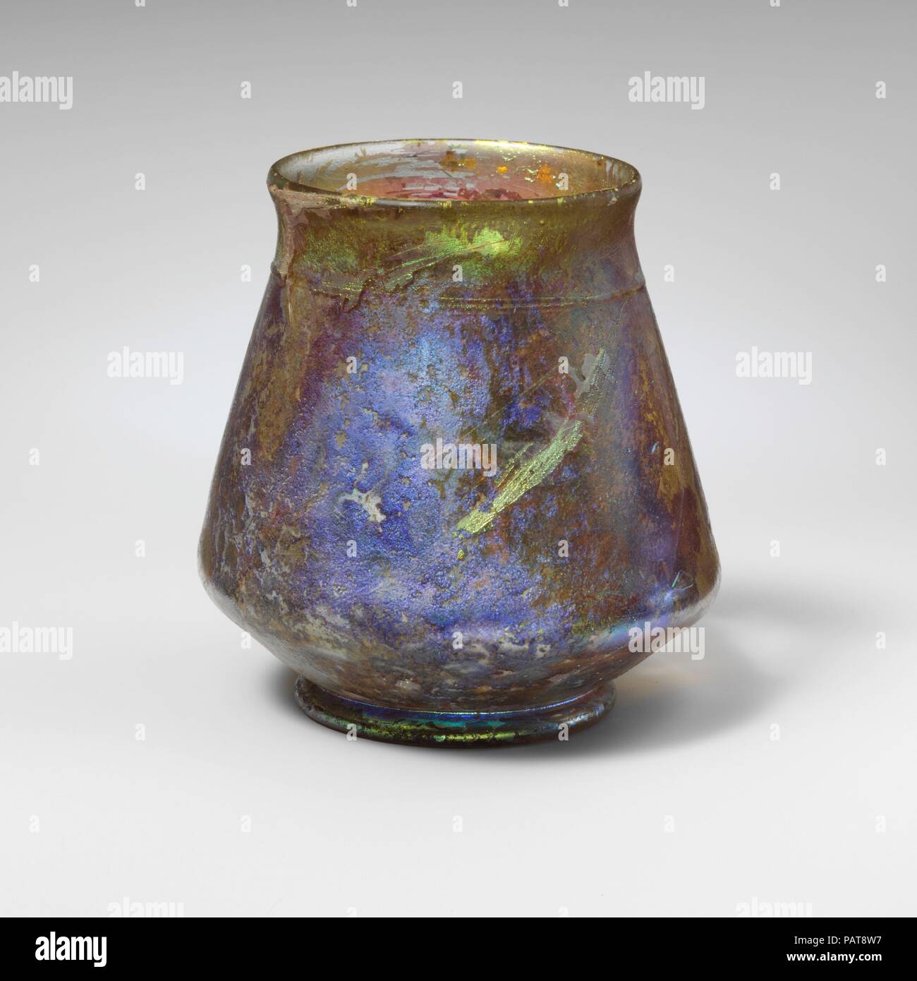 Glas Schale. Kultur: Roman. Abmessungen: 3 5/16 in. (8,5 cm) Durchmesser: 3 1/4 x 2 1/4 in. (8,3 × 5,7 cm). Datum: 2.-3.Jh. N.CHR.. Farblos mit grünlichen Tönung, mit Trail im gleichen Glas. Glatte, abgerundete Kante; kurz, abfackeln Hals; carinated Körper mit geraden, konischen Seiten, dann schräg in die Integral, Tubular Base Ring; breite, flache Unterseite mit leichten kleinen zentralen Stoß. Einzigen horizontalen Strecke rund um den Oberkörper, dann Spirale bis unten Rim zu beenden. Komplette, außer für große Loch in der Seite; viele Pinprick blasen; stark verwitterte und narbige, mit brillanten Schillern; einige Boden encrustatio Stockfoto