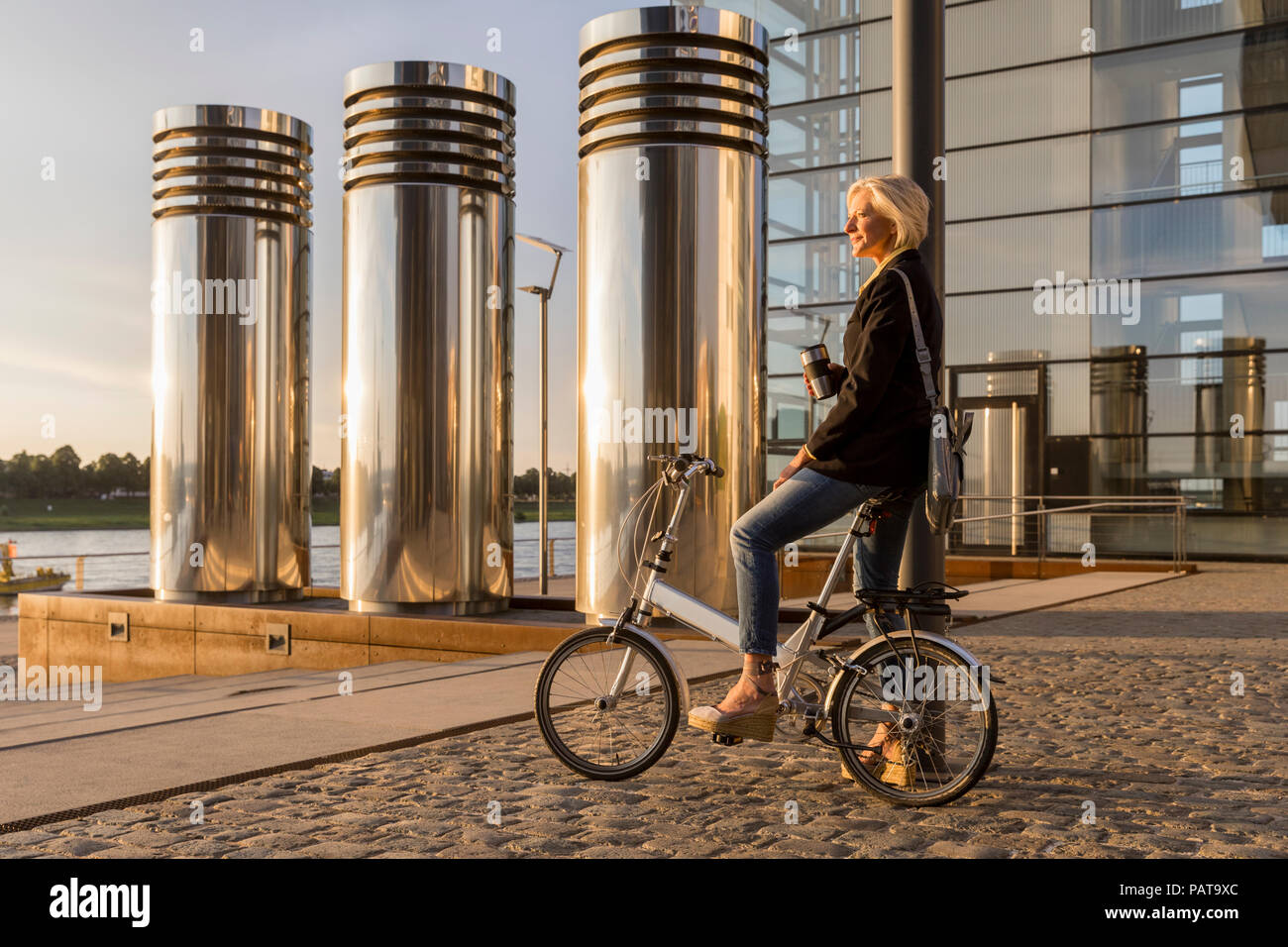 Ältere Frau mit Takeaway Kaffee und City Bike mit einer Unterbrechung bei Sonnenuntergang Stockfoto