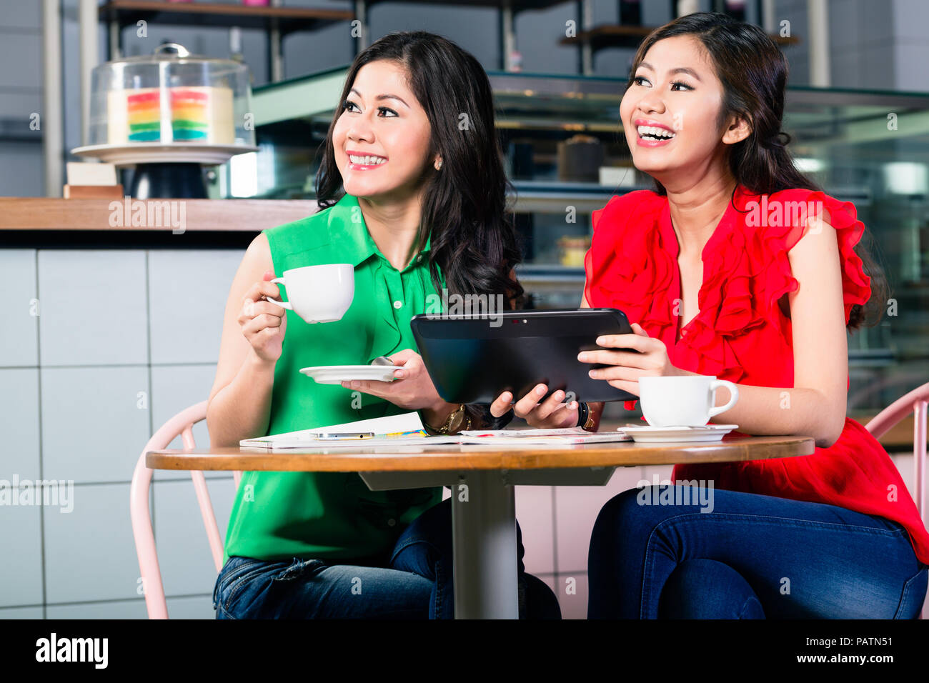 Zwei schöne Frauen, die zusammen einen Tablet-PC bei einer Tasse Kaffee Stockfoto