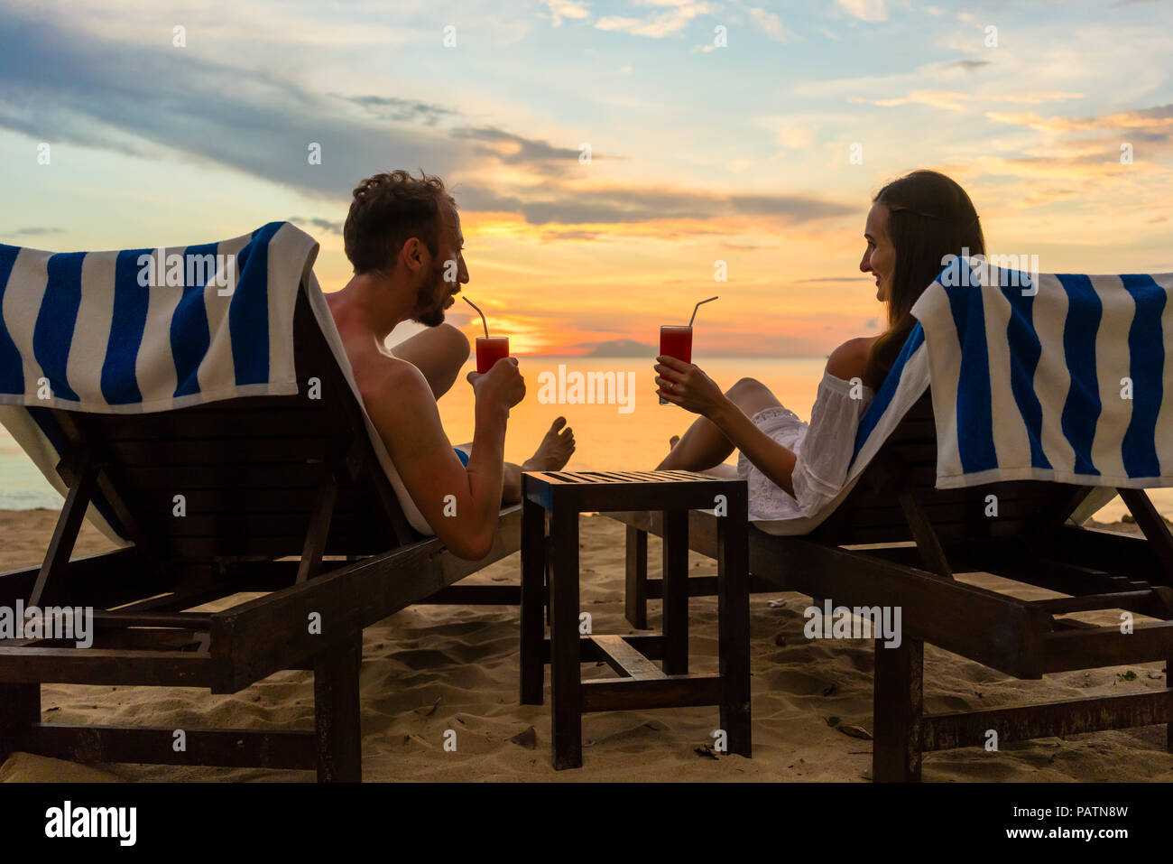Junges Paar trinken Cocktails am Strand bei Sonnenuntergang während der Ferien Stockfoto