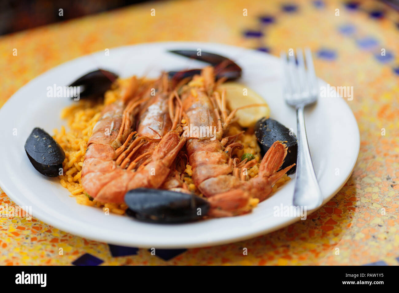 Royal Paella. Lecker Reis mit Riesengarnelen und Muscheln auf weißer Teller mit Gabel Stockfoto