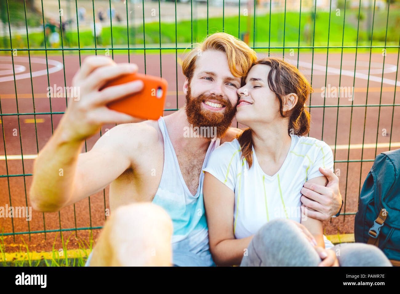 Ein mans Paar rote Haare und Bart und Frau Erholung nach Sport im Freien auf Gras im Hintergrund des Stadions. Der Kerl hält red Smartphone auf outstre Stockfoto