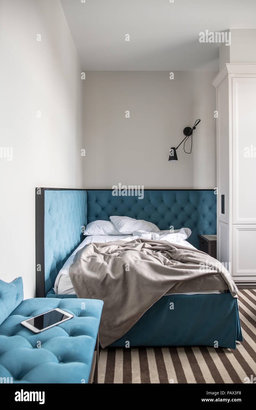 Stilvolle Zimmer in einem Hotel mit hellen Wänden und einem gestreiften Stock. Es ist ein blauer Doppelbett mit weißer Bettwäsche und einem grauen Bettdecke, dunkelgrau Nachttisch Stockfoto
