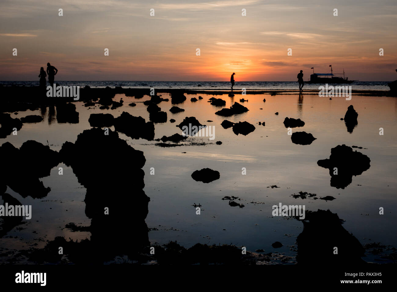 Silhouetted felsigen Strand Szene mit Einheimischen und Touristen sammeln Seesterne und Seeigel bei Ebbe sunrise - Malapascua - Philippinen Stockfoto