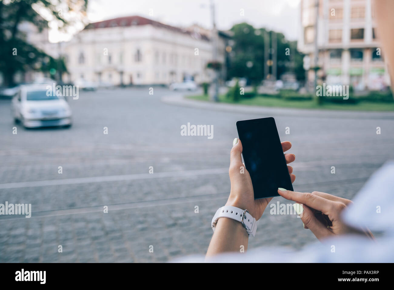 Rückansicht unkenntlich junge Frau mit Smart Phone in der Nähe von europäischen Pflasterstein Straße mit Autos. Close-up weibliche Hände berühren Gerät Geröll Stockfoto