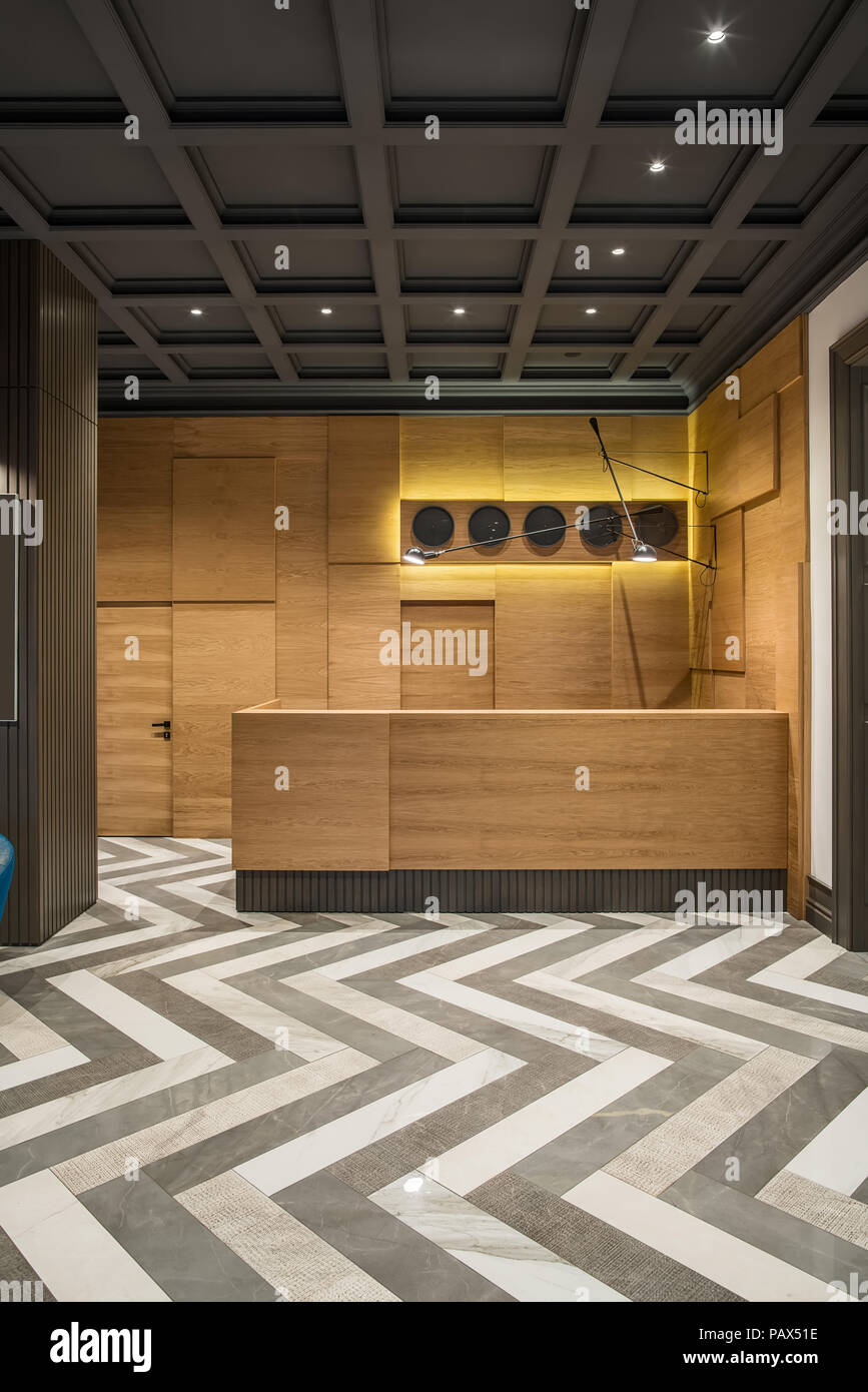 Interieur mit leuchtenden Lampen im Hotel mit dunklen Decke und gemusterten Fliesenboden. Es ist eine hölzerne Rezeption mit mehreren schwarzen Uhren und Hangi Stockfoto