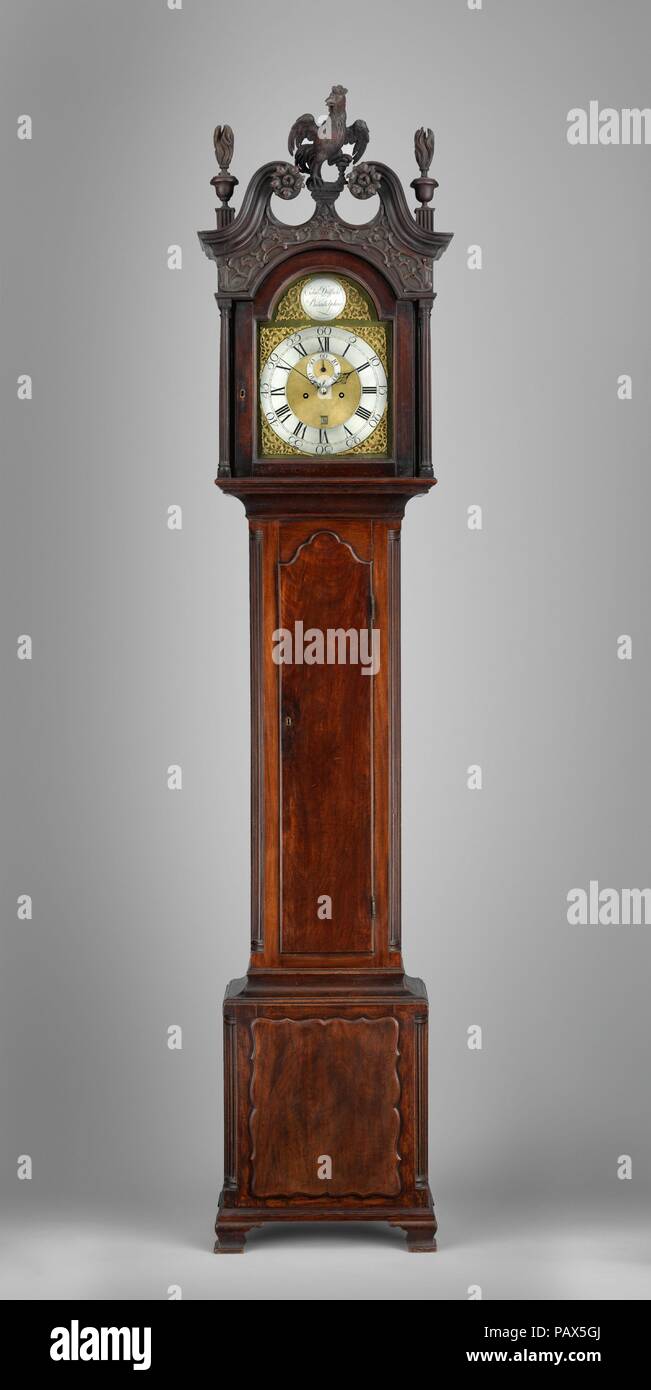 Tall-Case Uhr. Kultur: American. Abmessungen: 8 ft. 9 in. × 19 cm. × 10 cm. (266,7 × 49,5 × 26,7 cm). Schöpfer: Edward Duffield (American, 1720-1801). Datum: 1765-80. Diese Uhr verfügt über ein ausgeklügeltes Gewicht - angetriebene Bewegung, die für acht Tage läuft und Glockenspiel auf die Stunde. Seine Mahagoni, mit kunstvollen Schnitzereien und Applikationen, besitzt einen Hahn Kartusche oben - ein Motiv häufig auf Englisch und Französisch Uhren gesehen, aber selten auf amerikanische Beispiele. Der Hahn kann eine Referenz an den Apostel Petrus, dem Schutzpatron der Uhrmacher, oder an der letzten Christi Verkündigung Stockfoto