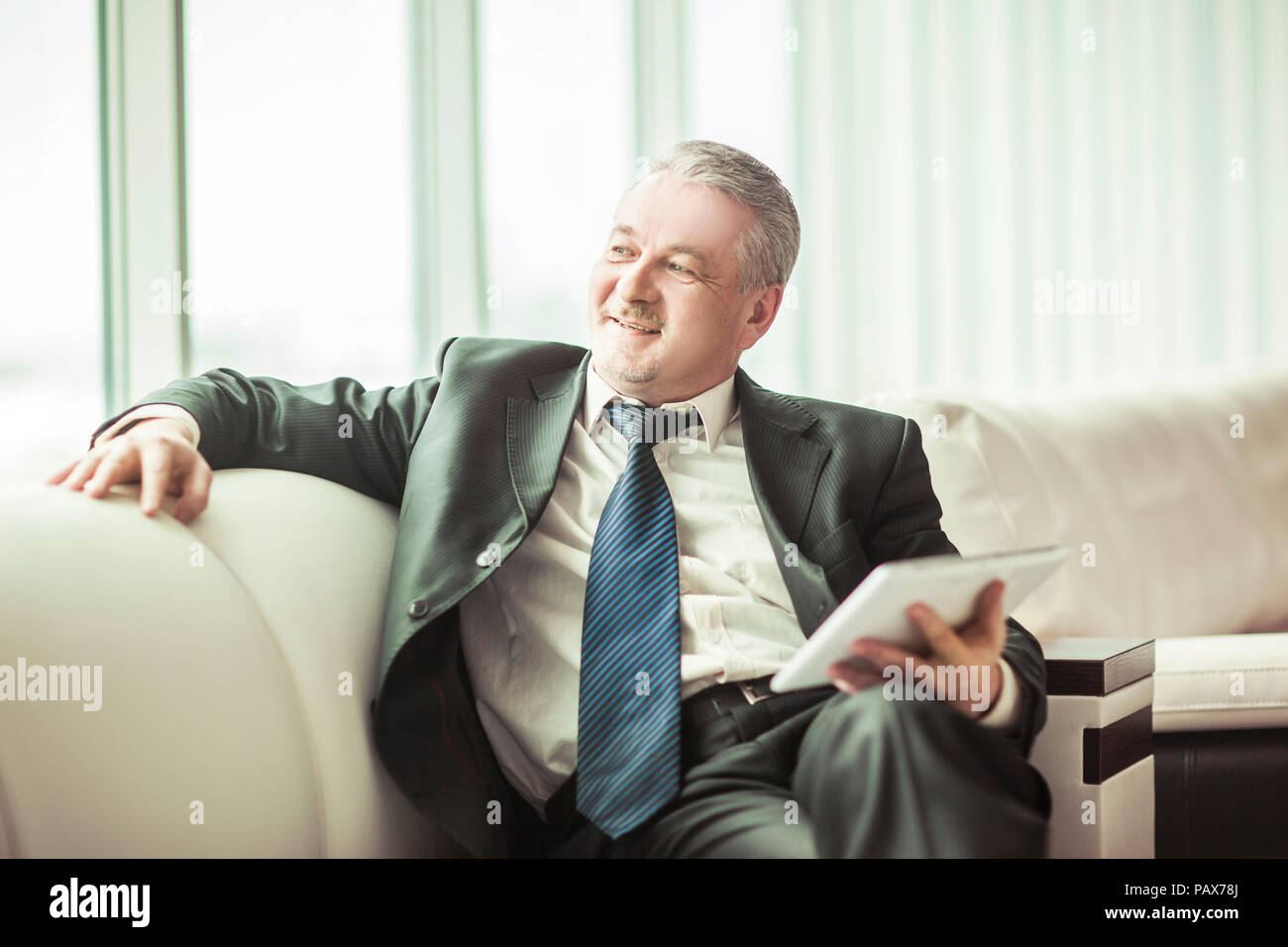 Erfolgreicher Geschäftsmann mit digitalen Tablet auf dem Sofa sitzen im eigenen Büro Stockfoto