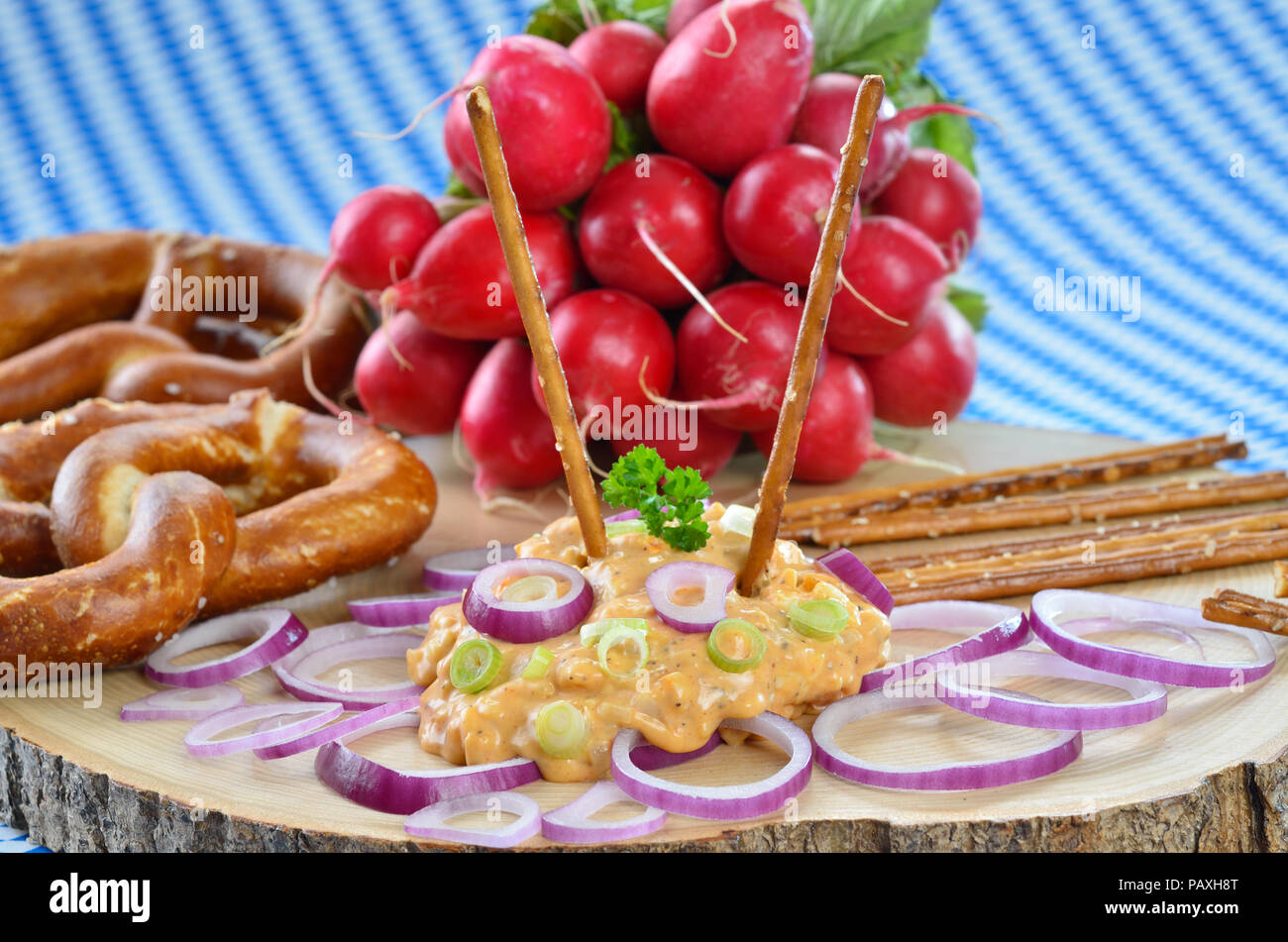 Bayerische Käsespezialität "obazda", serviert mit Zwiebelringen, Brezeln und Radieschen auf einem hölzernen Platte Stockfoto