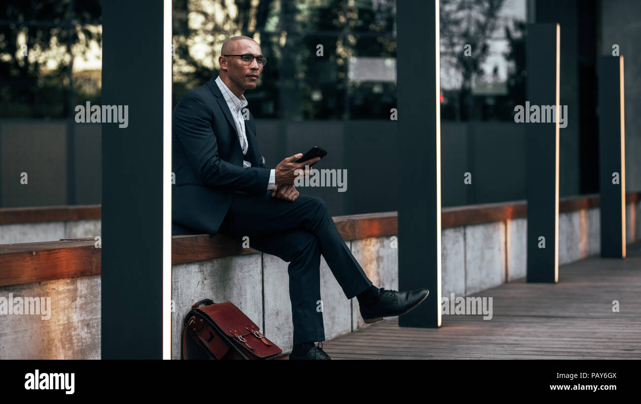 Unternehmer sitzen auf der Seite einer Straße mit seinem Handy und sein Büro Tasche an seiner Seite. Geschäftsmann Managing Business unterwegs sittin Stockfoto