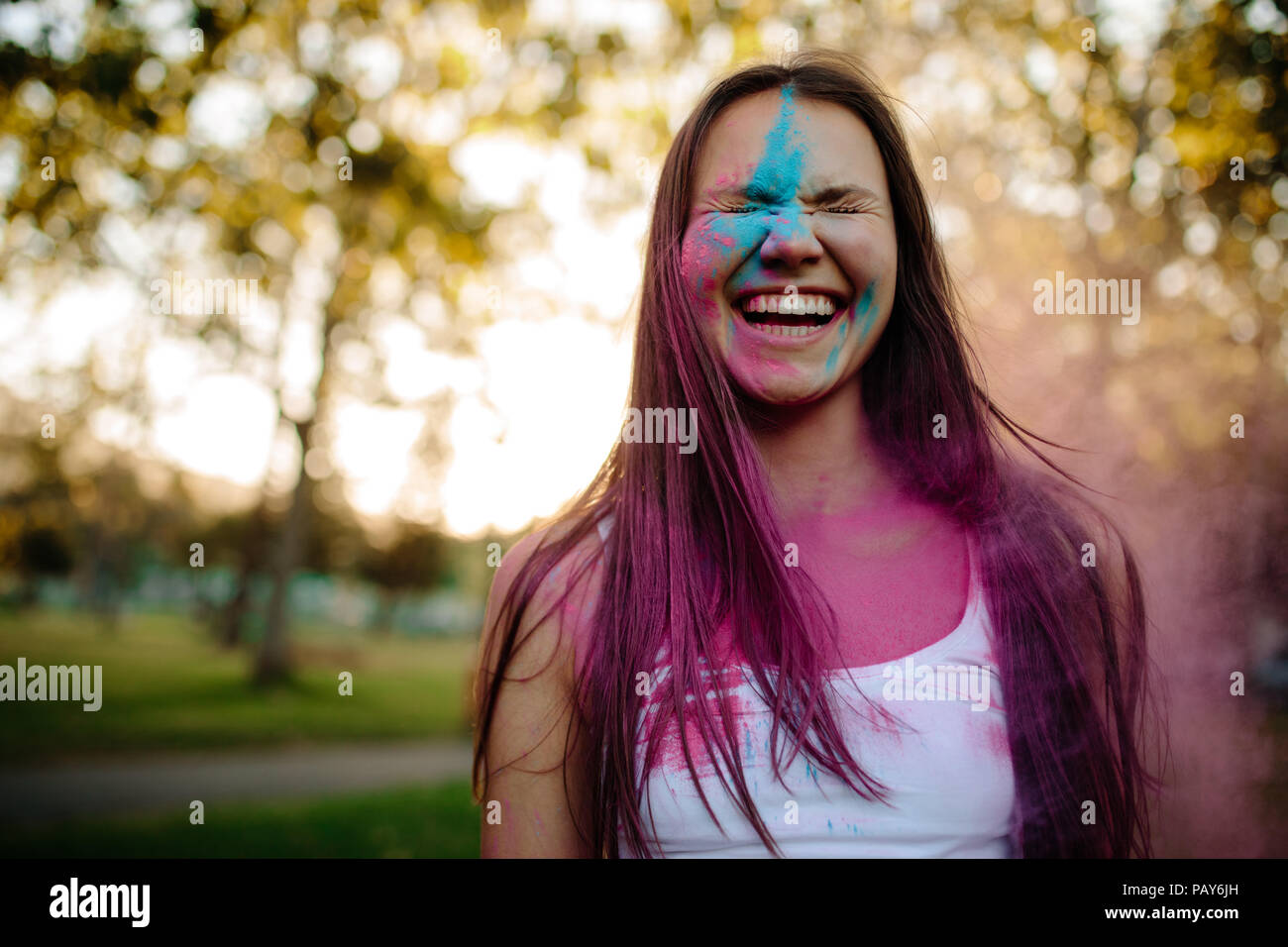 Porträt eines lächelnden jungen Frau mit Gesicht mit Farbe verschmiert. Fröhliches Mädchen im Park mit farbigem Pulver auf ihrem Gesicht. Stockfoto