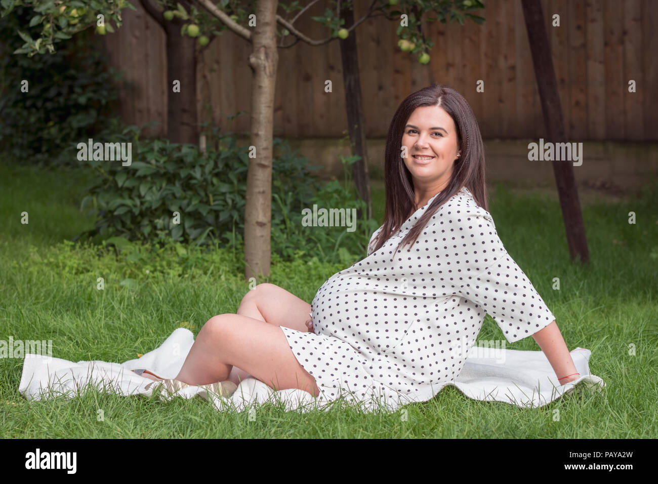 Junge schwangere Frau sitzt im Garten auf der Wiese Stockfoto