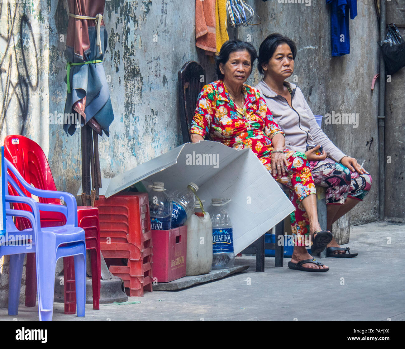Zwei vietnamesische Frauen sitzen auf Plastikstühlen gegen eine Wand in Ho Chi Minh City, Vietnam. Stockfoto