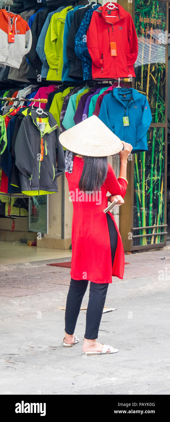 Rückansicht eines vietnamesischen Frau trägt ein rotes Oberteil und ein Stroh konische hat vor ein Geschäft mit Jacken in Ho Chi Minh City, Vietnam. Stockfoto