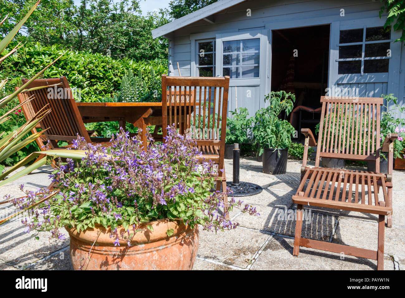 Graue Schuppen mit Blumen geschmückte Terrasse und Gartenmöbeln aus Holz Stockfoto