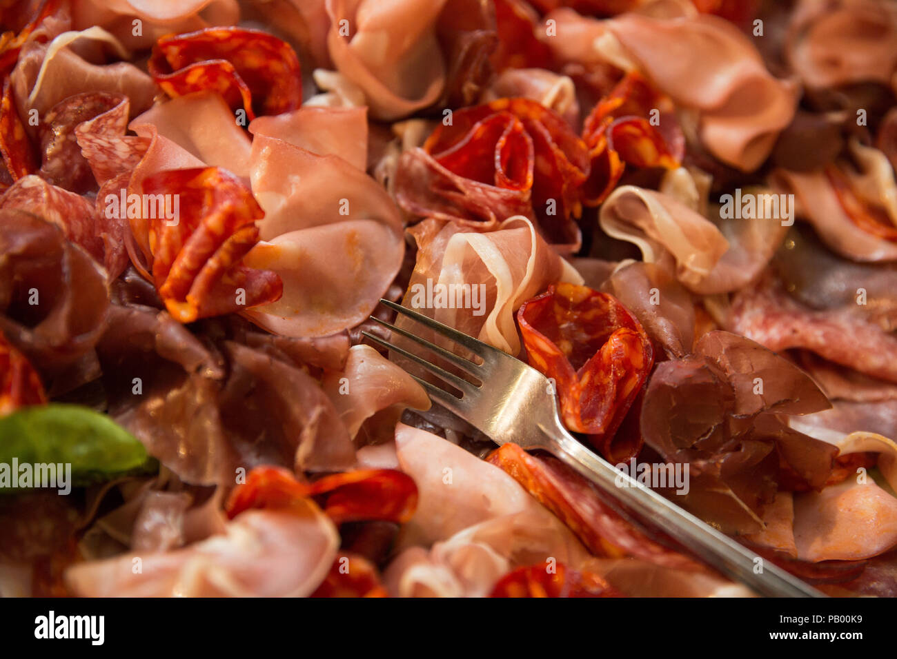 Nahaufnahme der verschiedenen Arten von italienischen Fleisch (ham) auf einem Teller mit der Gabel und ein Blatt Basilikum Stockfoto
